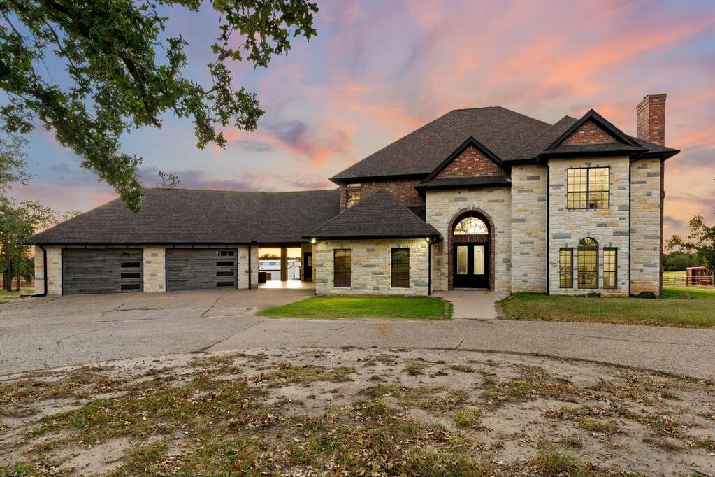 French country home with stone siding, roof with shingles, driveway, a chimney, and an attached garage