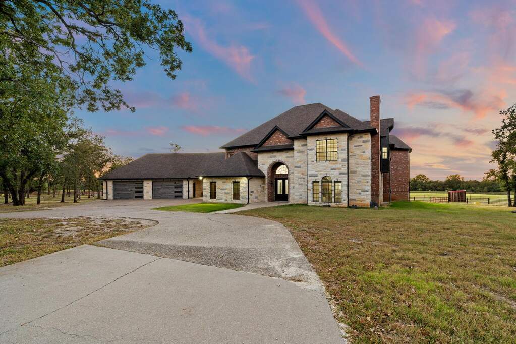 French country inspired facade featuring a chimney, stone siding, concrete driveway, and roof with shingles