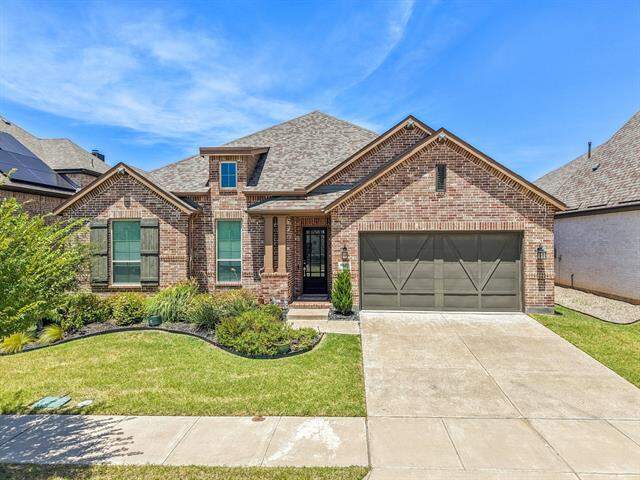 French country home with roof with shingles, concrete driveway, a garage, brick siding, and a front lawn