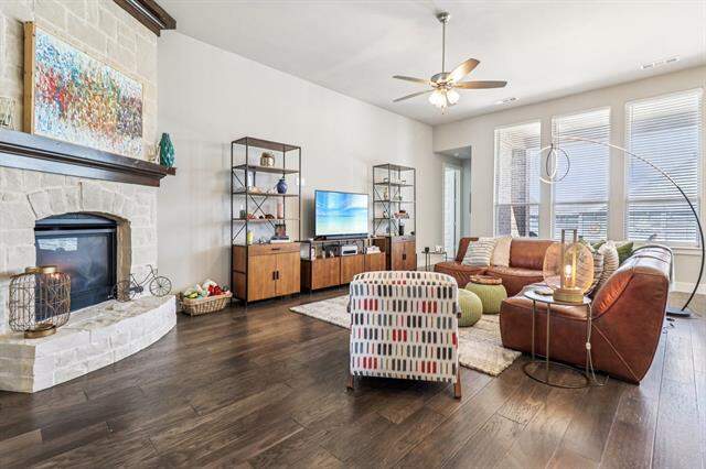 Living area with a stone fireplace, wood-type flooring, and a ceiling fan