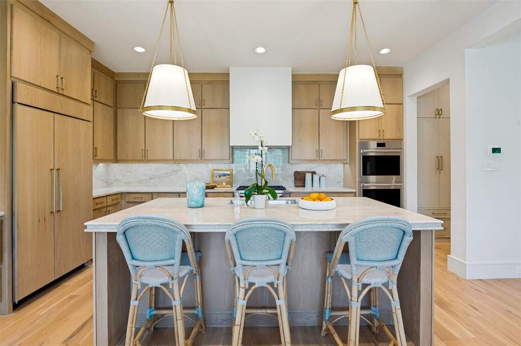 Gourmet kitchen featuring a large central island with a light-toned countertop, integrated panel-front refrigerator, stainless steel double ovens, custom wood-finish cabinetry, and wide plank