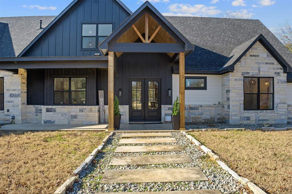 View of front facade with stone siding, covered porch, a front lawn, and board and batten siding
