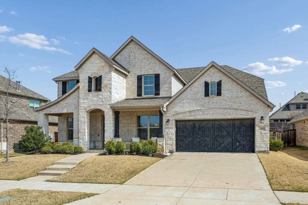 French provincial home with covered porch, concrete driveway, brick siding, stone siding, and roof with shingles
