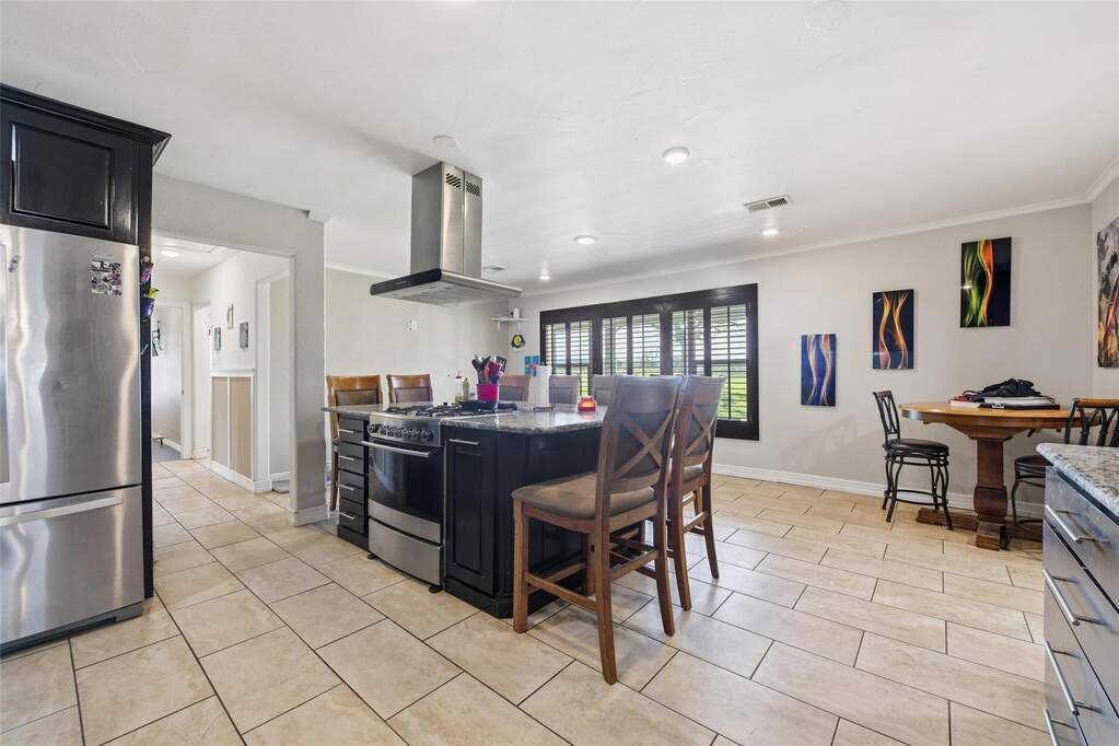Kitchen with dark cabinets, stainless steel appliances, island exhaust hood, dark stone countertops, and a kitchen island