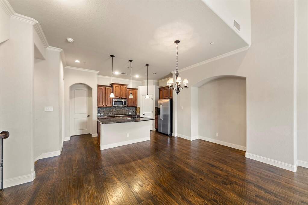 Kitchen with arched walkways, a kitchen island with breakfast bar and sink, open floor plan, crown molding, and stainless steel appliances.