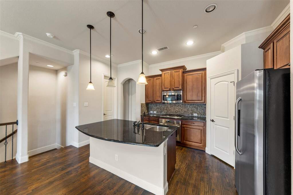 Kitchen with wood finish cabinets, stainless steel appliances, dark stone countertops, a kitchen island with sink, and crown molding