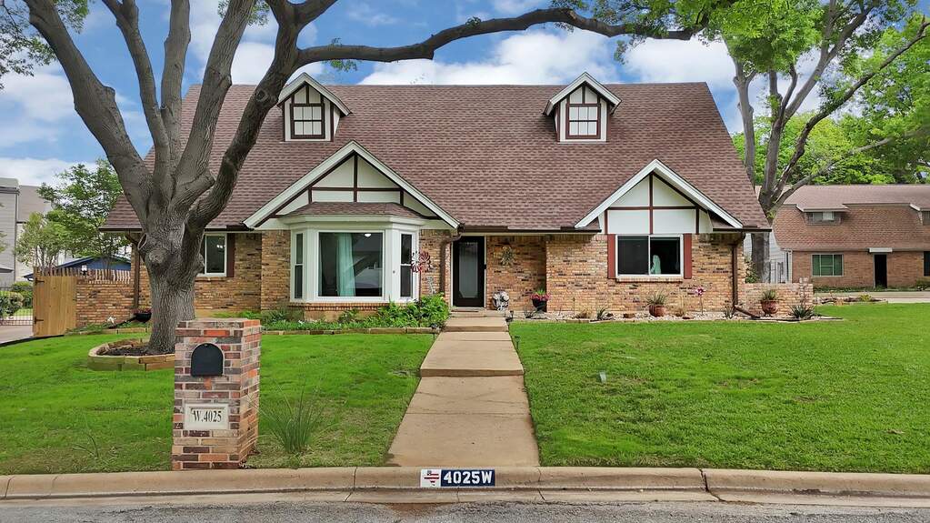 Tudor Cottage-style house featuring a front yard, roof with shingles, and brick siding