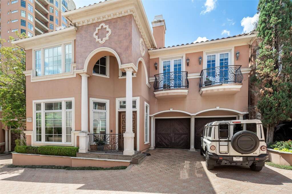 The property features a stucco exterior with decorative trim and columns, an arched entry, and a two-car garage with dark wood doors