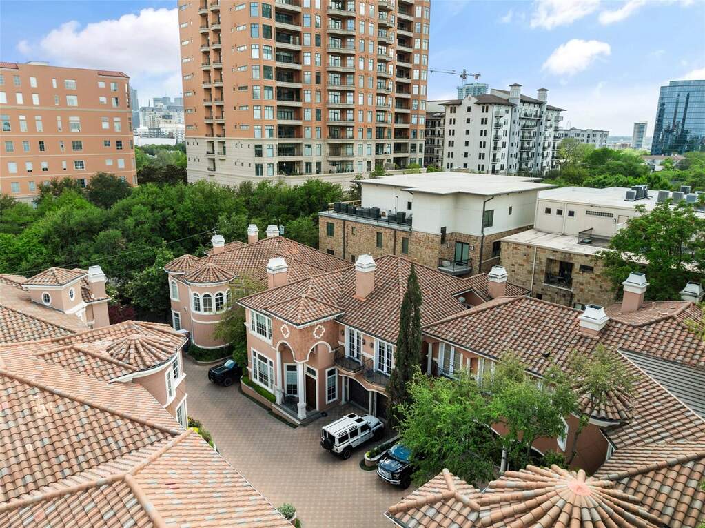 The property features a terracotta tile roof, a paved driveway, and established trees, set within a vibrant urban landscape