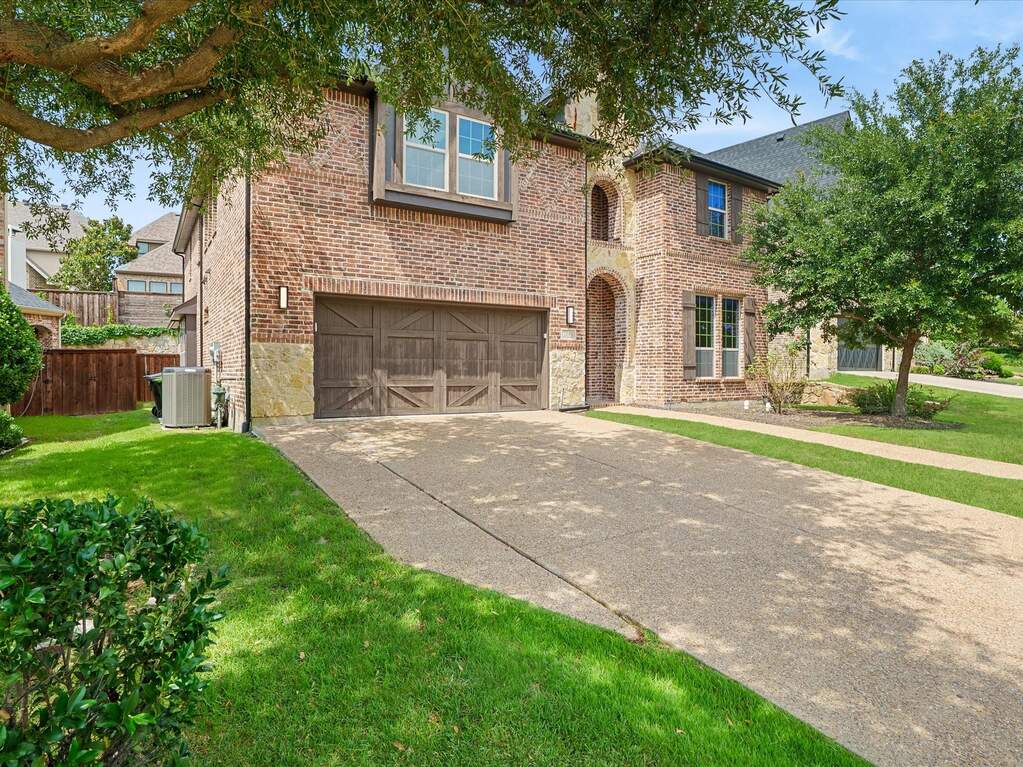 Brick and stone facade featuring an arched entry, a two-car garage with wood-finish doors, and a concrete driveway