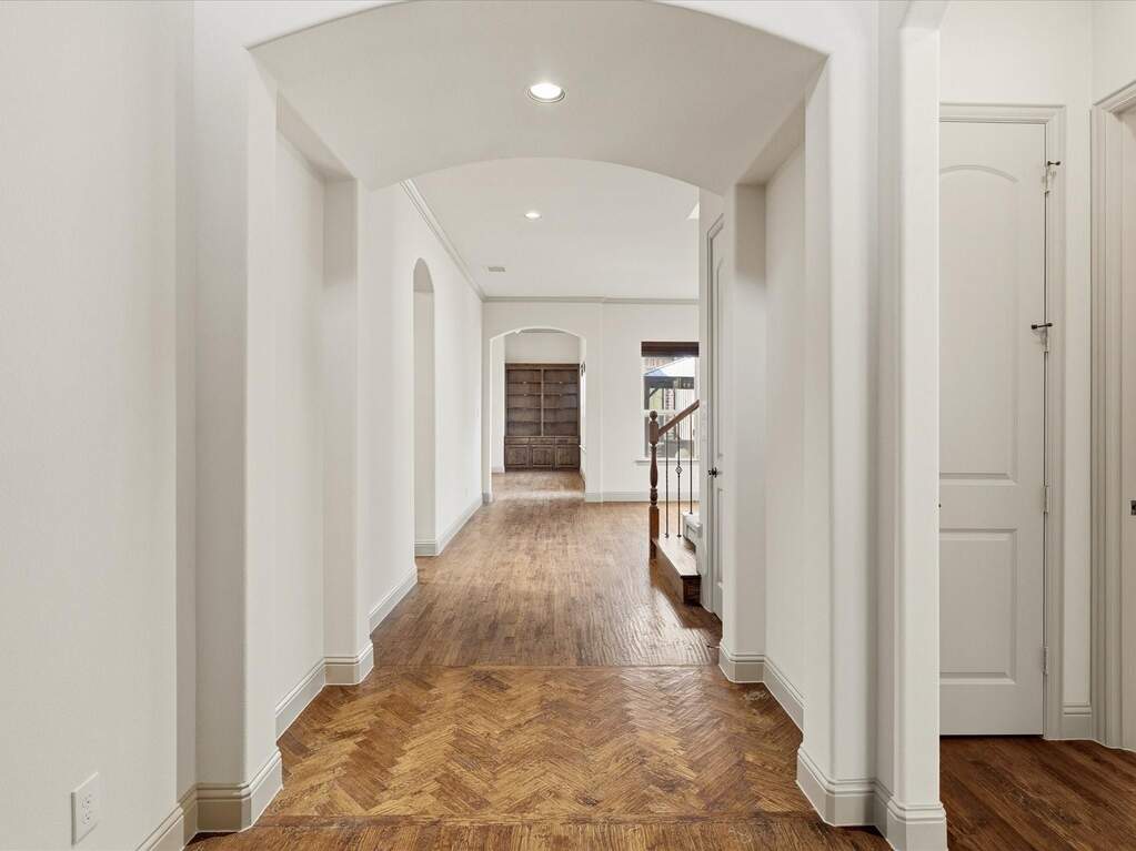 Hallway featuring herringbone wood-finish flooring, arched doorways, recessed lighting, and crisp white trim