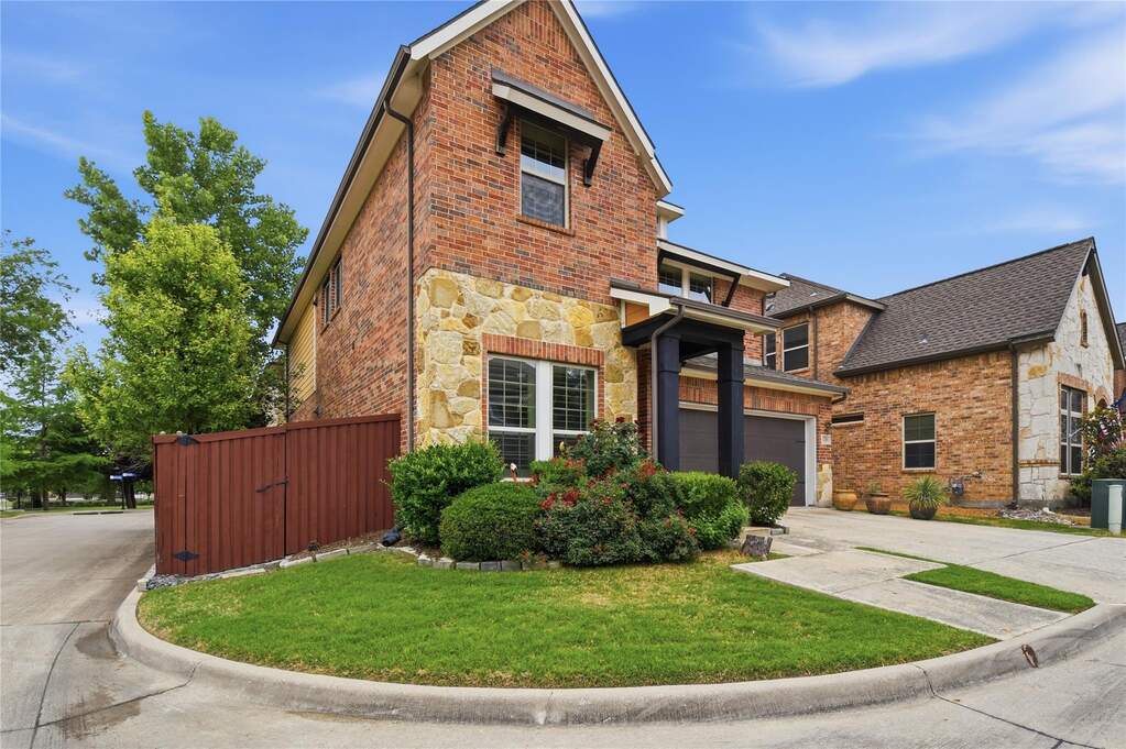 Brick and stone exterior featuring an integrated garage, covered entry, and established landscaping