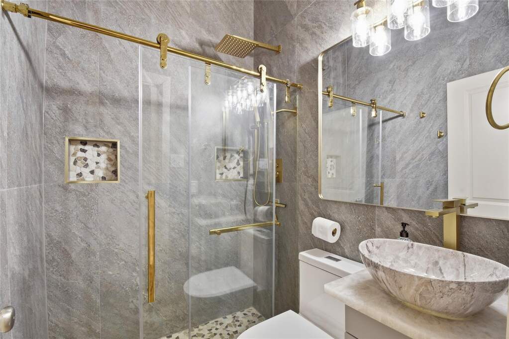 Full Guest bathroom Glass-enclosed shower with gold-tone hardware and a pebbled floor