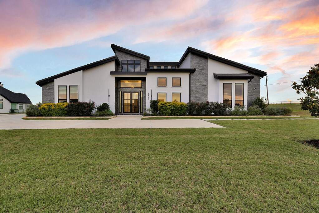 Contemporary exterior featuring a combination of white stucco and stone veneer, multiple black-framed windows, a prominent double-door entry, and a large front lawn