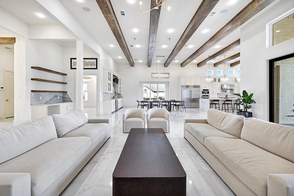 Spacious open-concept interior featuring vaulted ceilings with exposed wood beams, bright white walls, and large format tile flooring