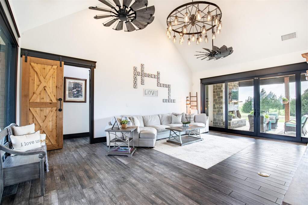 Spacious living area featuring vaulted ceilings, wood-finish flooring, and a large multi-panel glass slider opening to covered patio