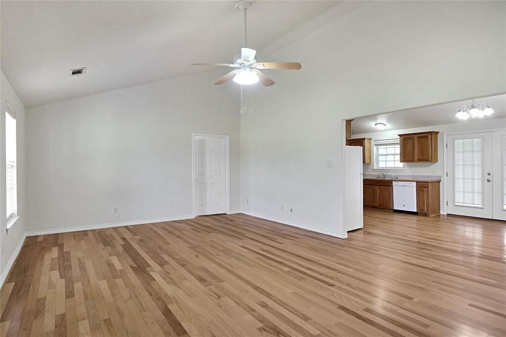 Expansive living area featuring vaulted ceilings, wood-finish flooring, and a ceiling fan with integrated lighting