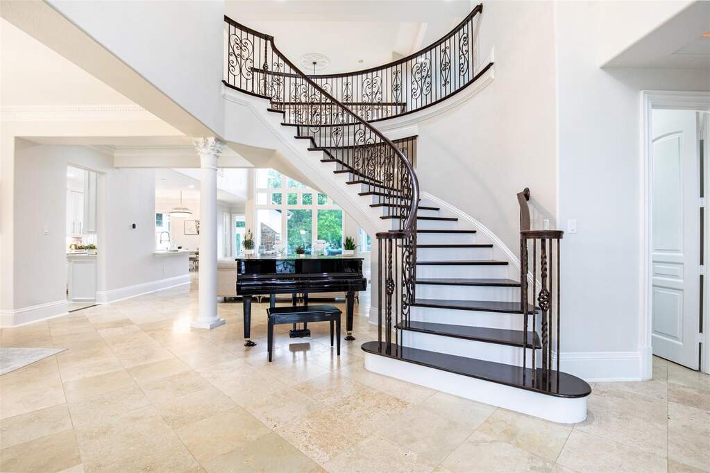 Grand two-story foyer featuring a curved staircase with wrought iron balusters and dark wood treads, light stone tile flooring, a decorative ceiling medallion, and a white architectural colum