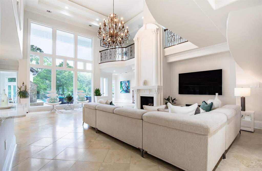 Two-story living area featuring a prominent fireplace, expansive window wall, grand chandelier, elegant open staircase, and tiled flooring