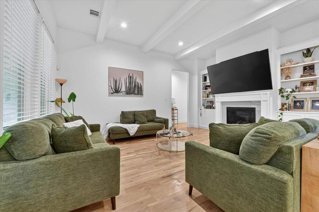 Spacious living area featuring vaulted ceilings with exposed beams, wood-finish flooring, and expansive windows