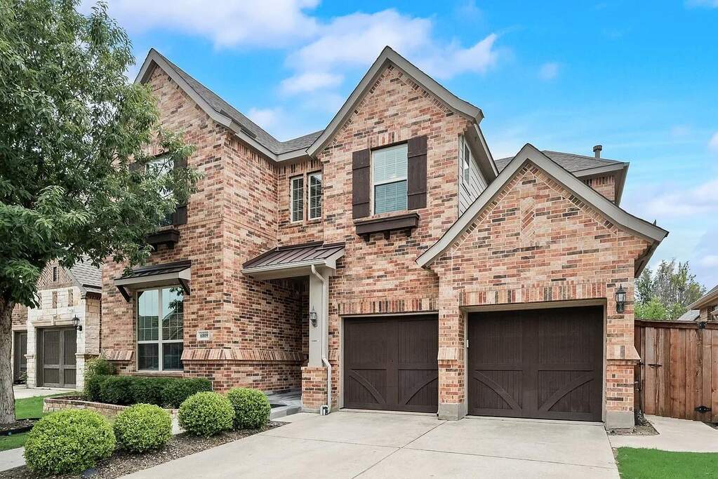 Two-story brick exterior featuring gabled rooflines, dark wood-tone garage doors, a covered entry, and a concrete driveway