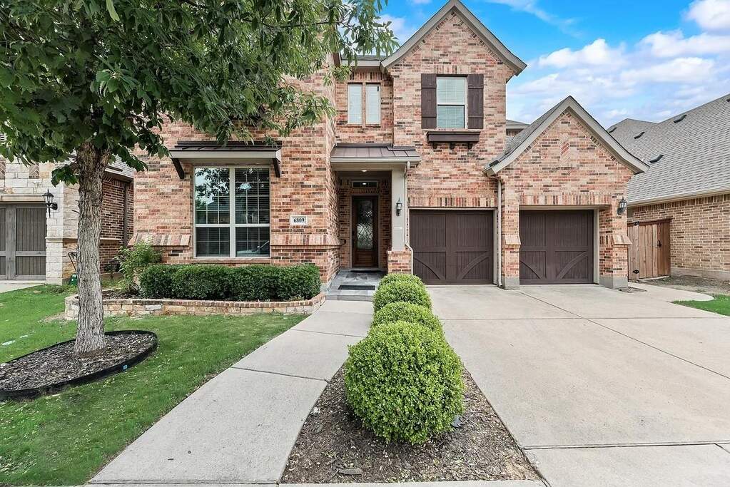 Brick and stone exterior featuring a two-car garage, established landscaping, and a covered entry