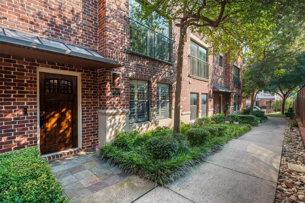 Brick exterior featuring a wood-paneled entry door with transom window detail, stone tile porch, decorative window shutters, and a metal awning