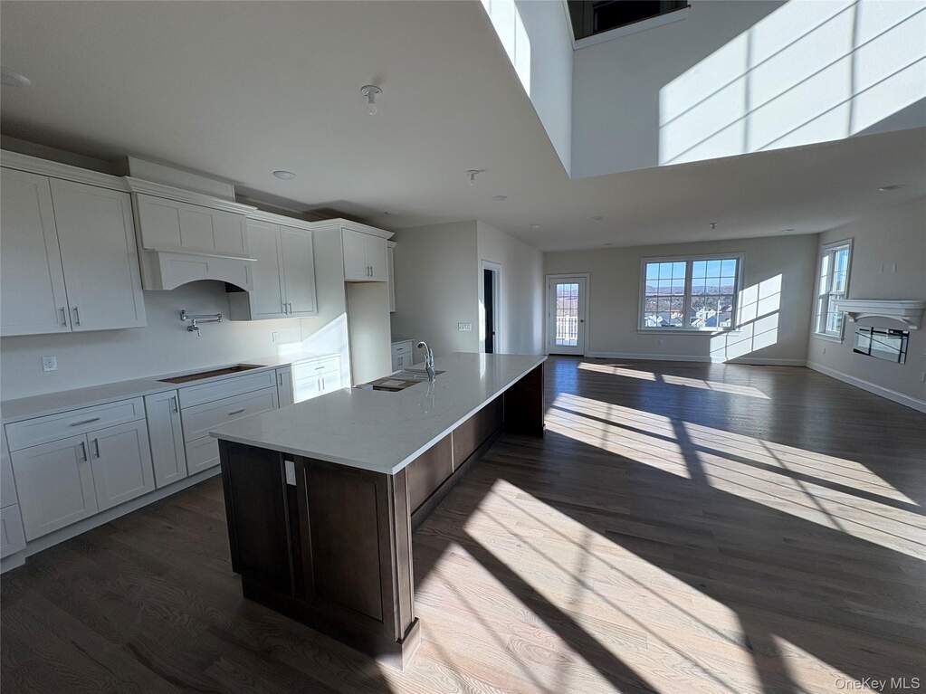 Kitchen featuring white cabinetry, an island with sink, dark wood-style flooring, light stone countertops, and a breakfast bar