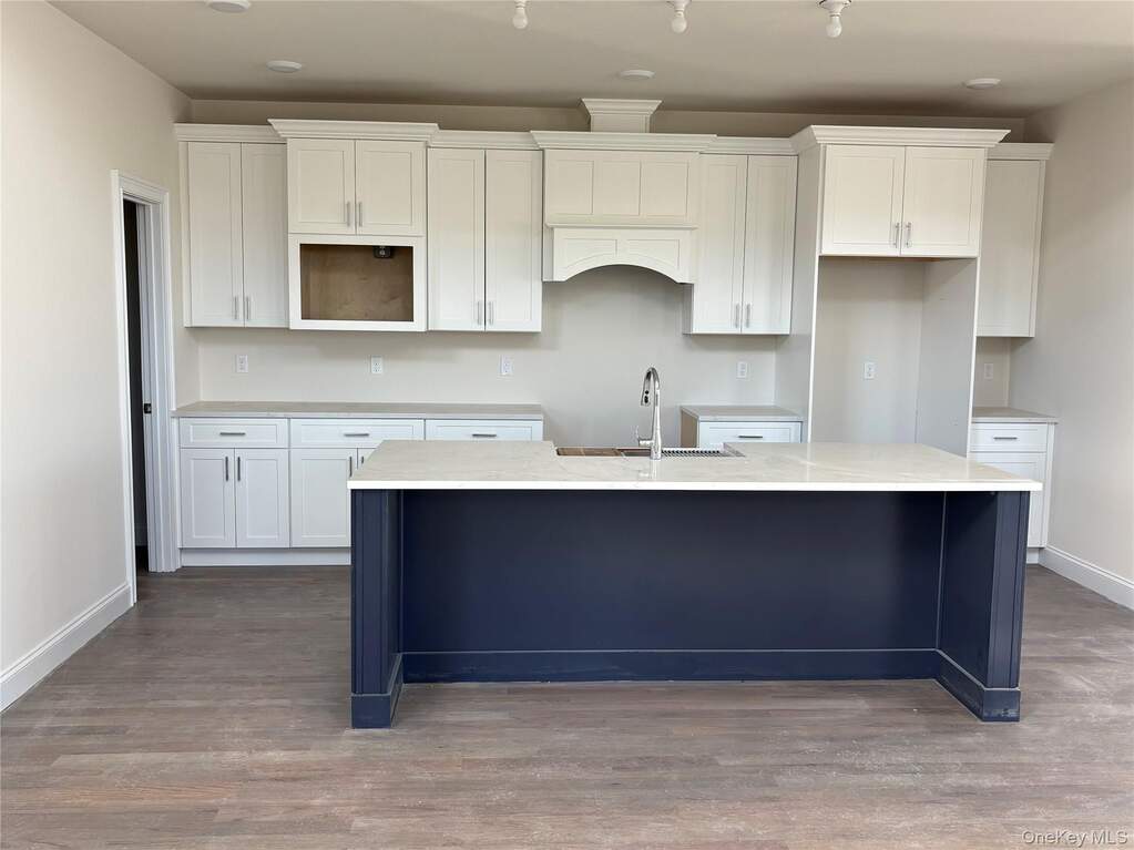 Kitchen featuring white cabinetry, light stone countertops, a center island with sink, and dark wood-style floors
