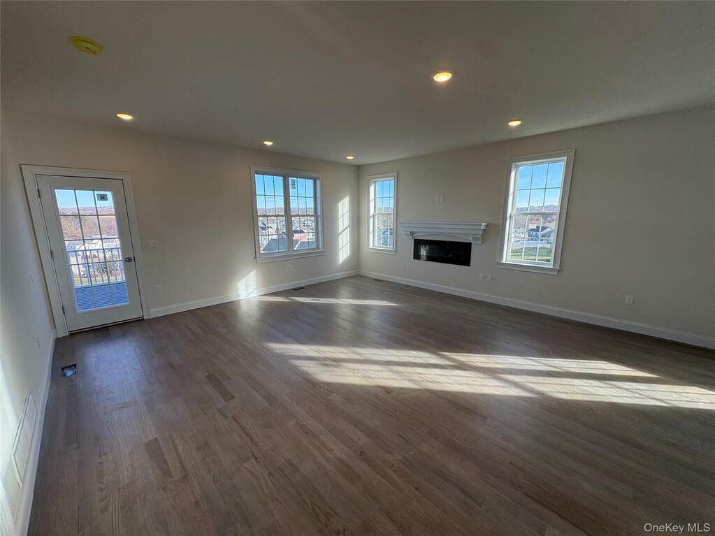 Unfurnished living room with recessed lighting, dark wood-style floors, a glass covered fireplace, and healthy amount of natural light