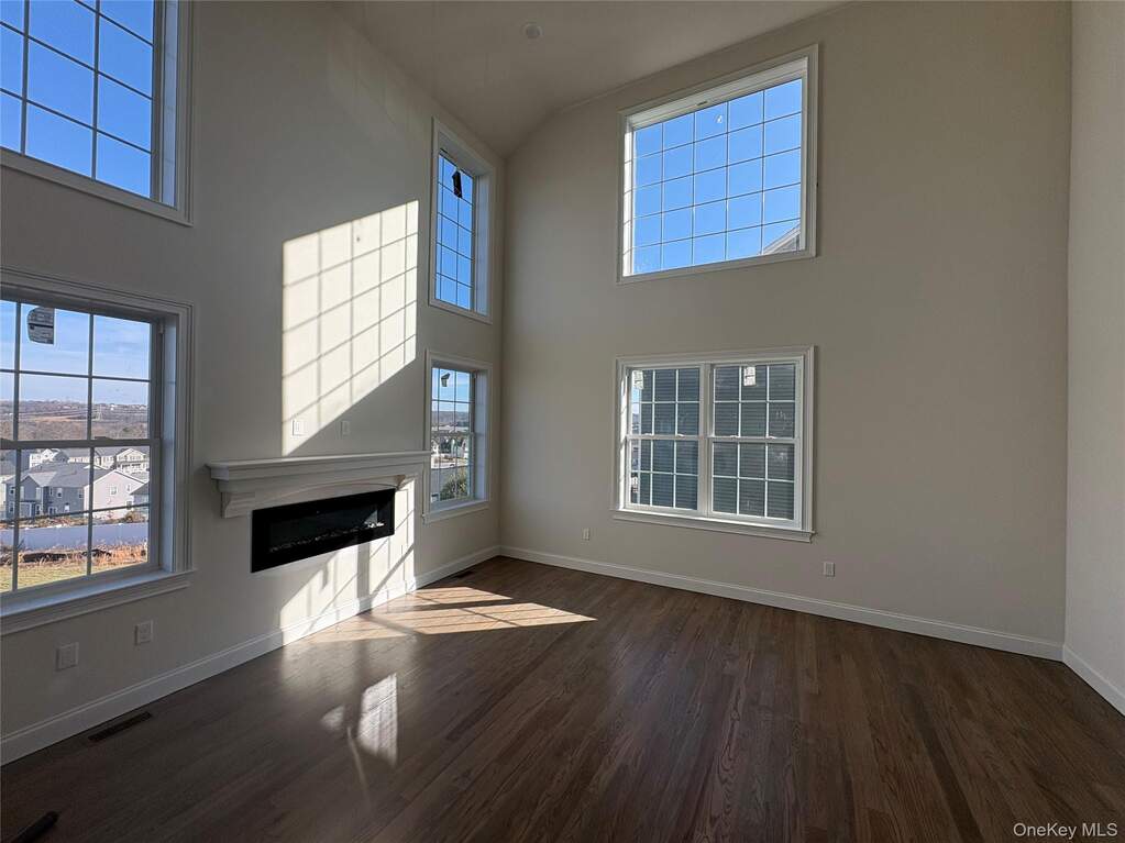 Unfurnished living room with a glass covered fireplace, dark wood-type flooring, and a high ceiling