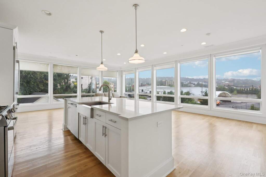 Kitchen featuring white cabinets, hanging light fixtures, gas range, light wood finished floors, and light stone counters