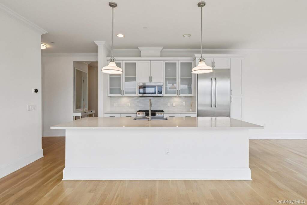 Kitchen featuring stainless steel appliances, ornamental molding, decorative backsplash, glass insert cabinets, and light wood-type flooring