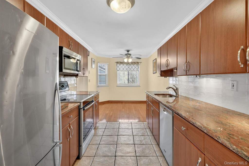 Kitchen with stainless steel appliances, light stone counters, wood finish cabinets, ornamental molding, and ceiling fan