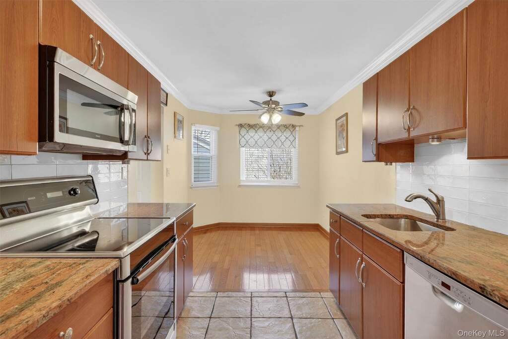 Kitchen featuring stainless steel appliances, wood finish cabinets, tasteful backsplash, crown molding, and light stone countertops