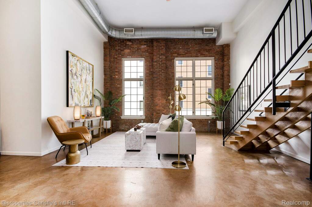 Living area with brick wall, a high ceiling, concrete flooring, and stairs