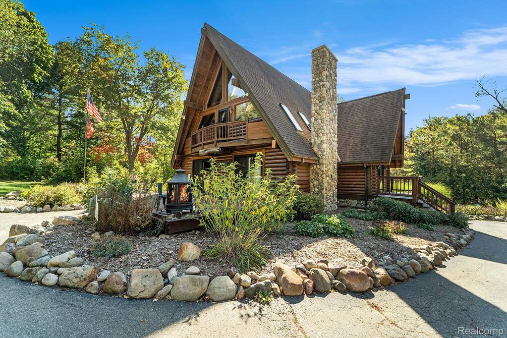 View of front facade featuring a shingled roof, a deck, a chimney, and log siding
