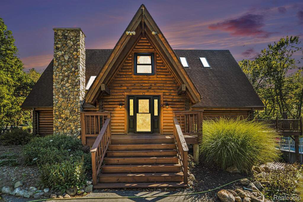 View of front of house with a shingled roof, a chimney, and log exterior