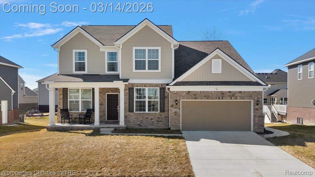 View of front of house featuring covered porch, a front yard, driveway, brick siding, and a shingled roof