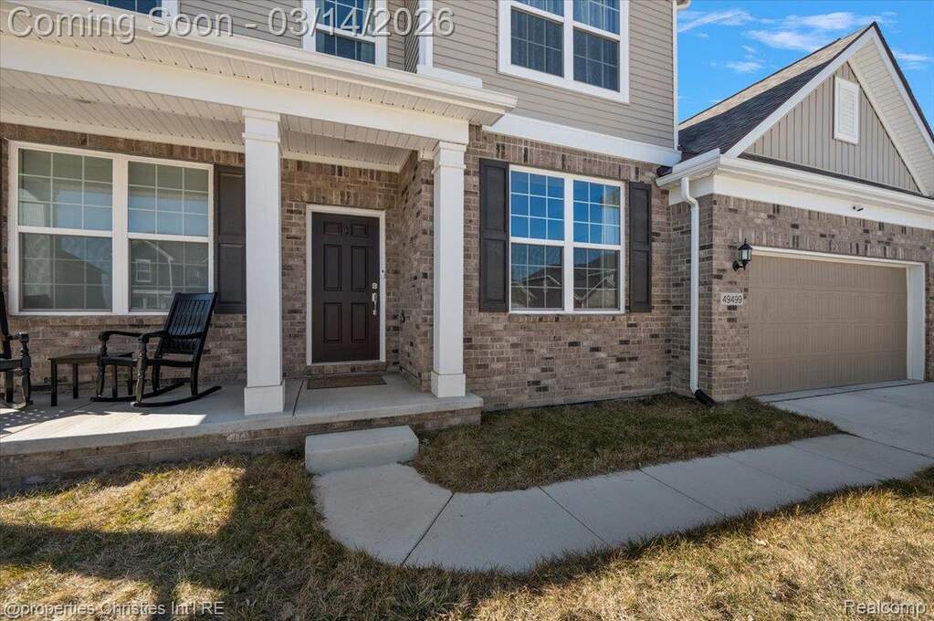 Entrance to property with covered porch, brick siding, a garage, and driveway