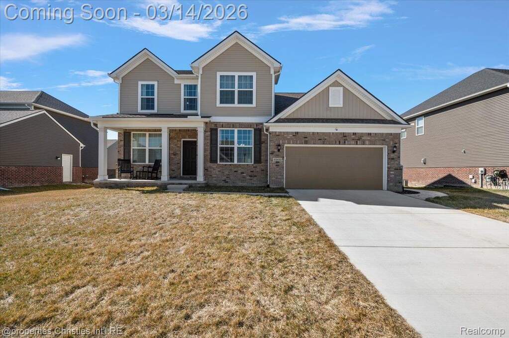 View of front of property with covered porch, driveway, an attached garage, brick siding, and a front lawn