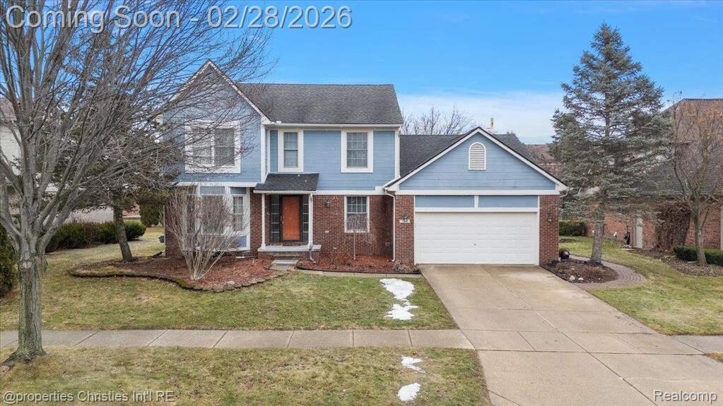 Traditional-style house featuring concrete driveway, brick siding, a front yard, and a garage
