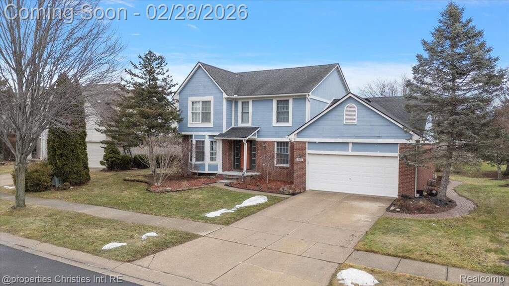 Traditional home featuring concrete driveway, brick siding, a front yard, and an attached garage