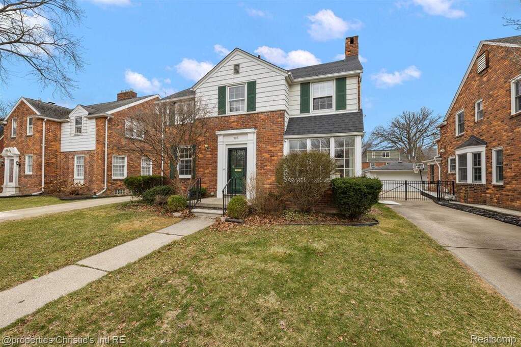 Traditional-style home featuring a chimney, brick siding, and a gate