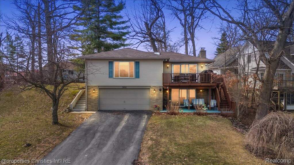 View of front facade with a patio area, driveway, a wooden deck, a yard, and a chimney
