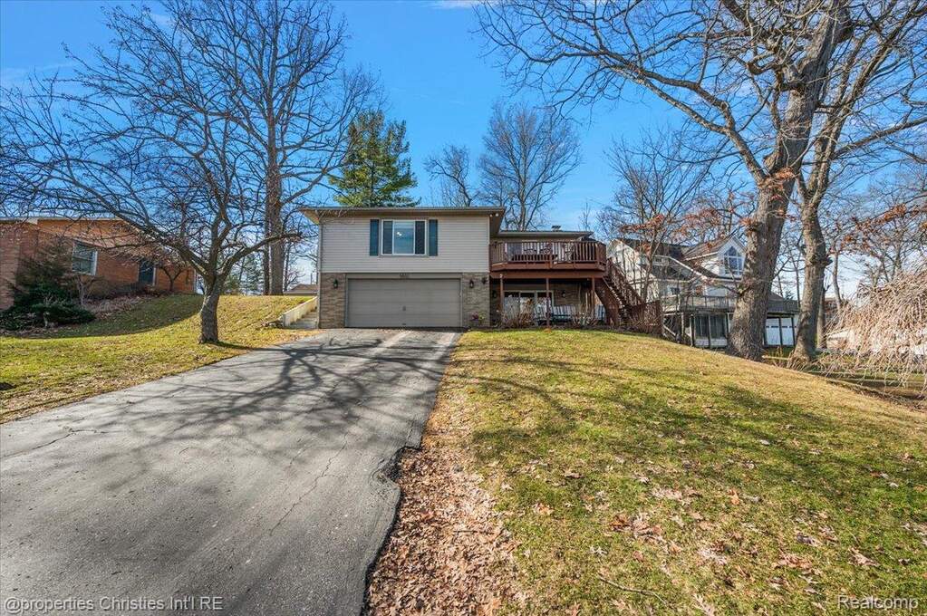 Traditional home featuring asphalt driveway, a garage, a front lawn, and a deck