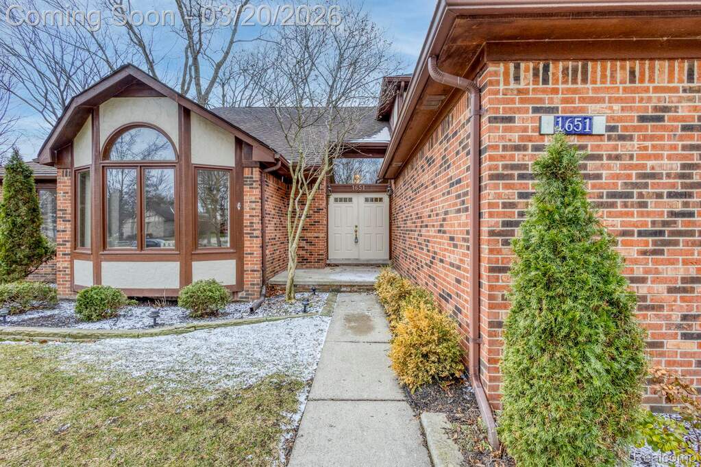 View of exterior entry with brick siding, roof with shingles, and stucco siding