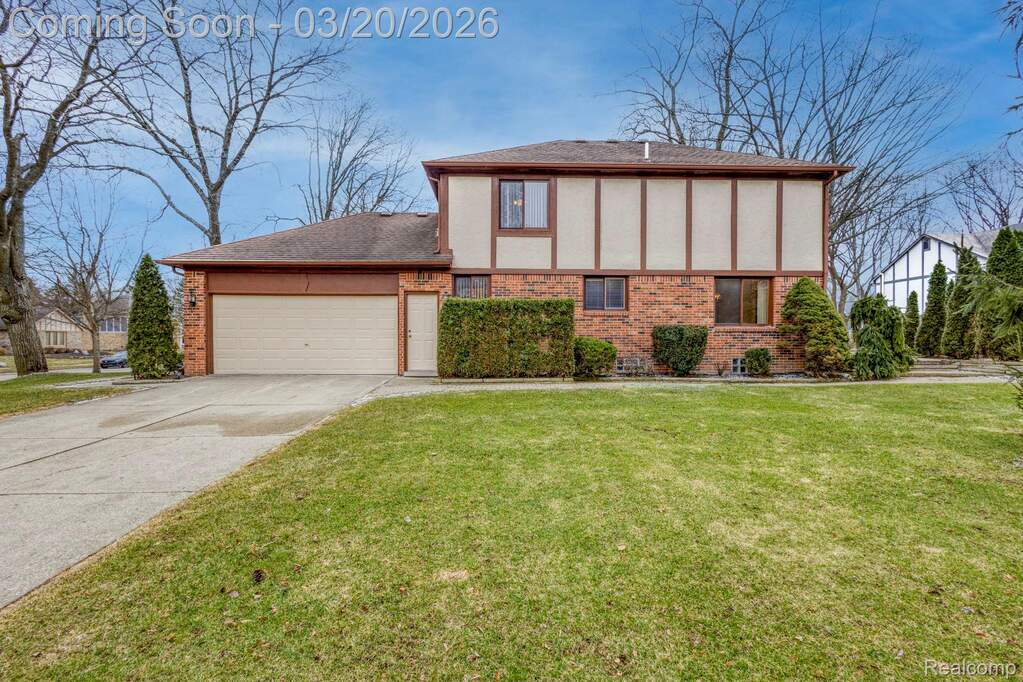 View of front of house with brick siding, an attached garage, stucco siding, a front lawn, and concrete driveway