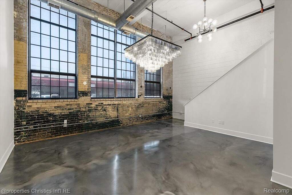 Unfurnished dining area featuring a high ceiling, brick wall, suspended lighting, and concrete flooring