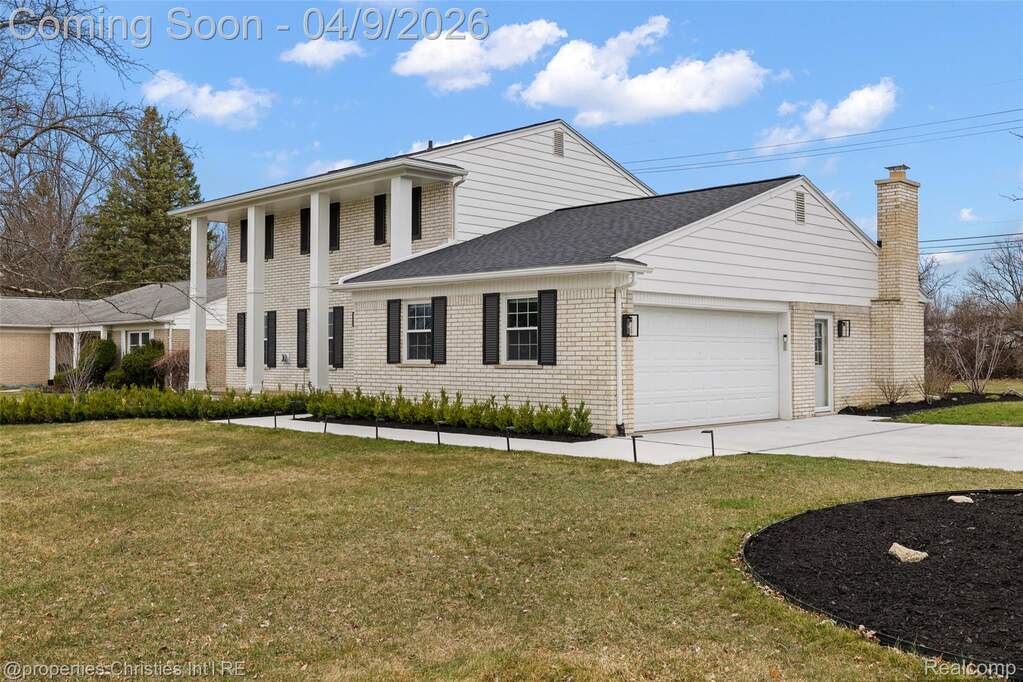Greek revival house with an attached garage, concrete driveway, a front yard, and brick siding